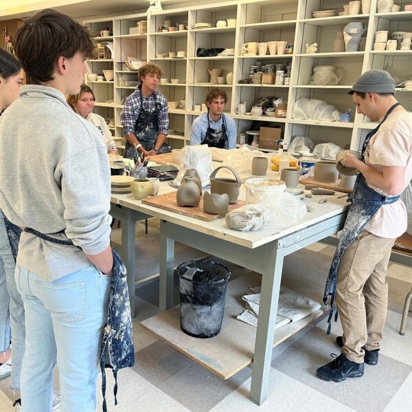 340172015_615329696766168_4318470699354313938_n student works on ceramics piece as students observe
