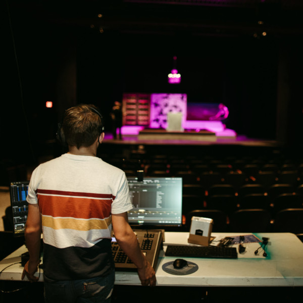 student at sound board in theater booth