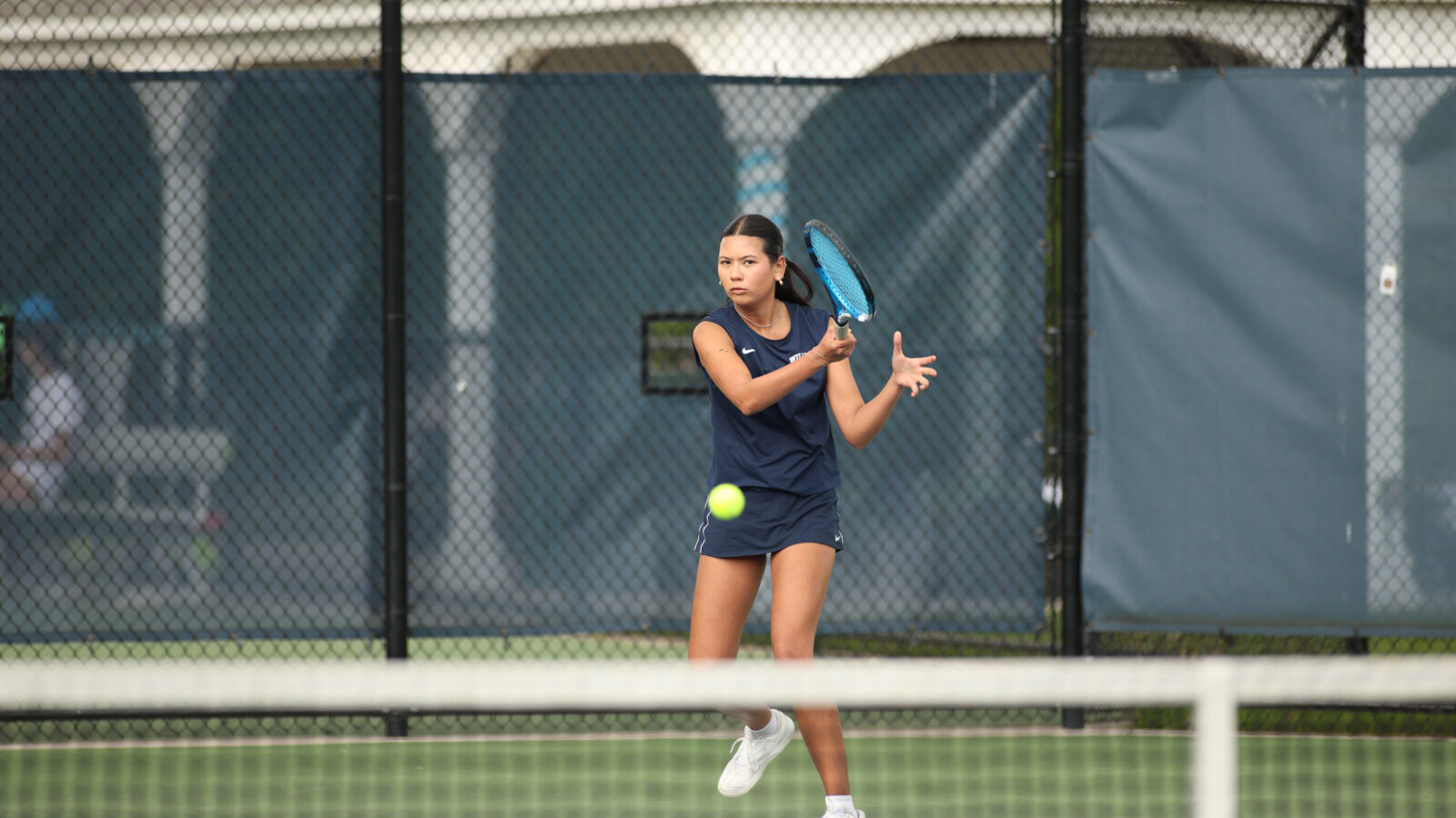 girl hitting tennis ball over a net