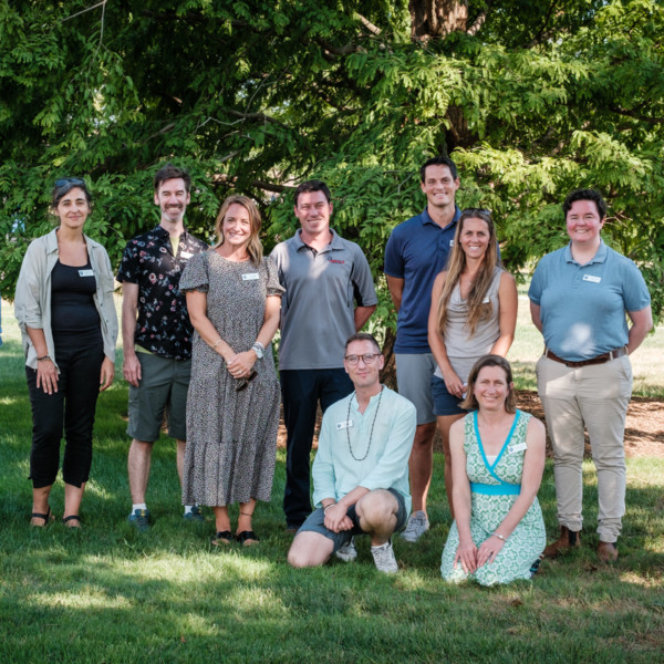 11 adults pose outside in the shade of a tree